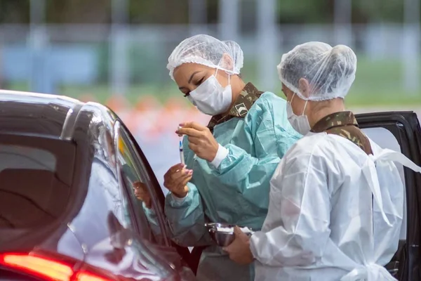 Mulheres com toca nos cabelos e máscara ao lado de carro preto
