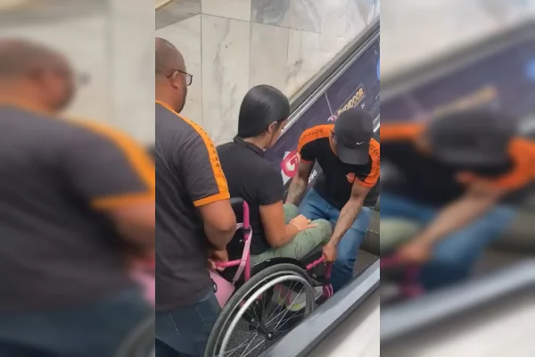 Imagem colorida de uma jovem sobre uma cadeira de rodas sendo carregada por dois homens