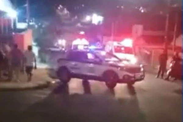 Uma viatura da polícia está atravessada em uma rua, com sirenes vermelhas e azuis ligadas; ao redor, mulheres observam - Metrópoles