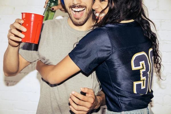 casal abraçado, a mulher usando uma camisa de time na moda tendência blokecore date encontro - metrópoles