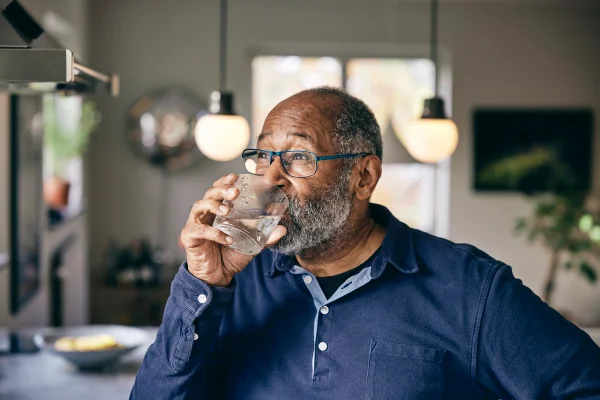 Imagem mostra idoso negro de camisa social azul, bebendo um copo de água - Metrópoles