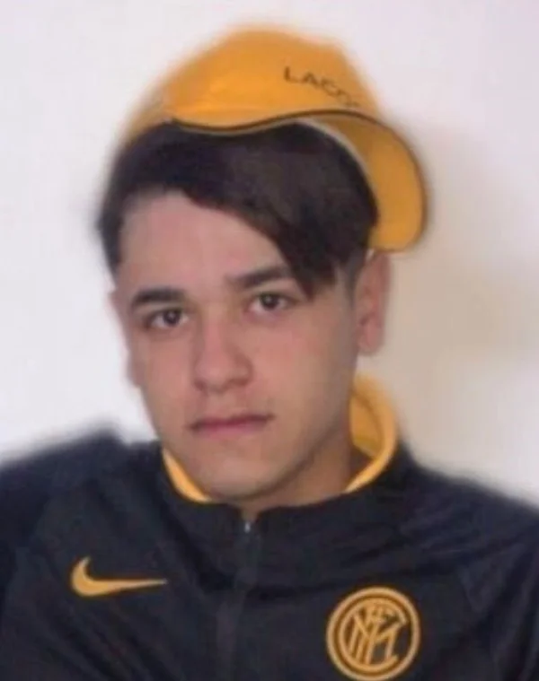 Jovem de expressão séria usa jaqueta preta e boné laranja.