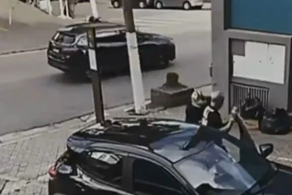 Imagem colorida mostra bandido abordando o pai do cantor MC Gui para roubar o carro em um estacionamento no Tatuapé, zona leste de São Paulo