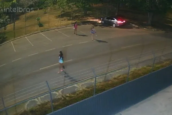 Imagem colorida gravada por câmeras de segurança mostra três mulheres andando em rua, próximas a carro