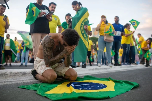 Foto de um homem ajoelhado em uma bandeira do Brasil