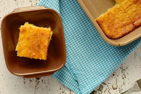 Bolo de tapioca cortado dentro de uma travessa marrom sobre a mesa e toalha de mesa azul - Metrópoles