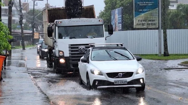 Imagem colorida de veículos passando em rua alagada chuva de montanha - Metrópoles