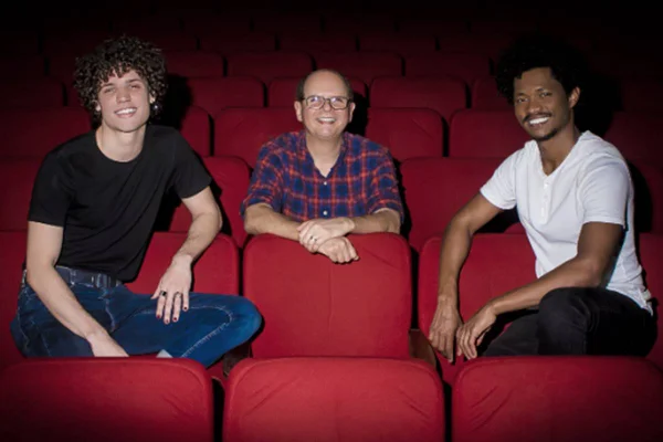 Foto colorida de Carlos Jardim com dois homens sentados ao seu lado - Metrópoles
