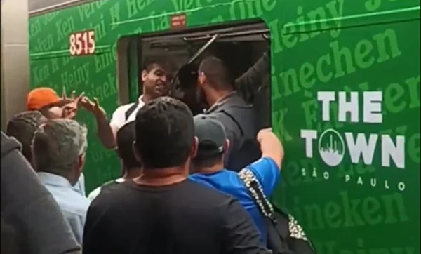 Em foto colorida homem de caliseta branca argumenta com segurança da ViaMobilidade na entrada de um vagão, no qual há a logo do festival The Town - Metrópoles