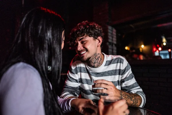 Jovem casal conversando em um bar. Conceito de flerte, paquera. Metrópoles