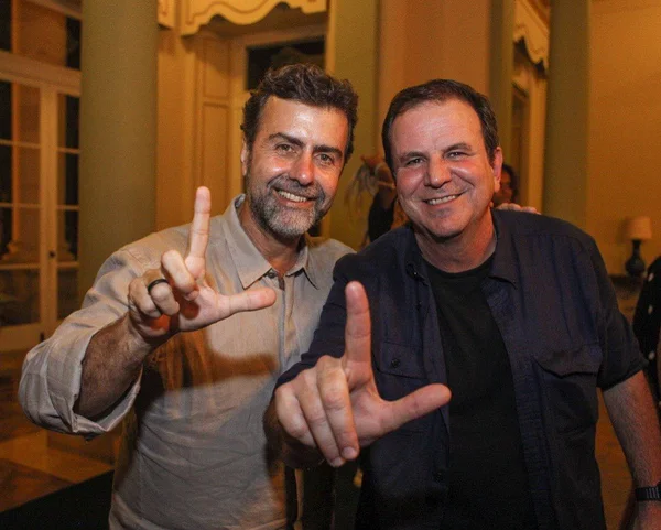 imagem mostra marcelo freixo e eduardo paes fazendo um gesto de L com as mãos, em alusão ao nome de Lula