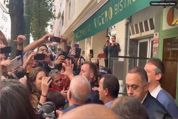 O presidente eleito Lula é recebido por apoiadores em durante almoço em Lisboa. Na imagem, ele é cercado por diversas pessoas que tiram fotos em entrada de restaurante com toldo verde - Metrópoles