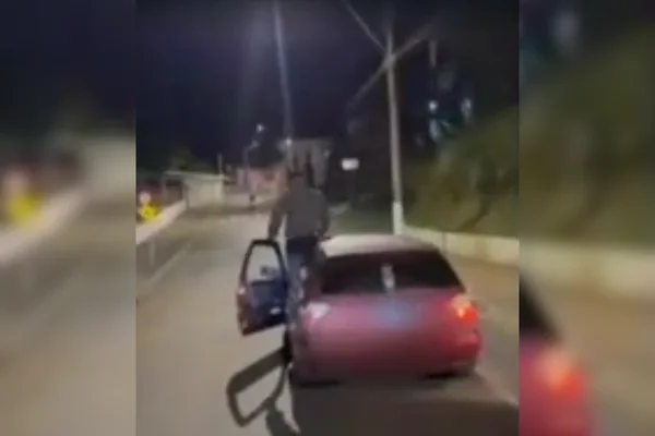 Imagem colorida de um adolescente subindo no teto de um carro e caindo no meio da rua - Metrópoles