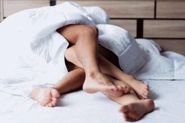 quatro pernas entrelaçadas em cima de uma cama