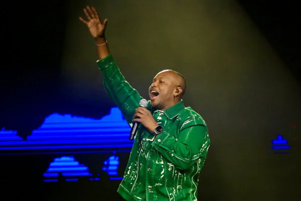 Foto colorida de Thiaguinho cantando no palco vestindo uma roupa verde - Metrópoles