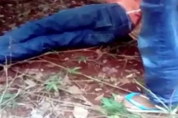 O jovem está deitado no chão com uma calça jeans e uma blusa vermelha