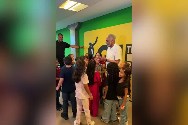 Imagem colorida mostra Gilberto Gil com alunos de escola municipal. Metrópoles