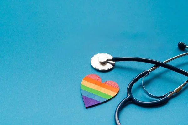 Estetoscópio e um coração lgbt em fundo azul. Conceito de saúde lgbt. Metrópoles