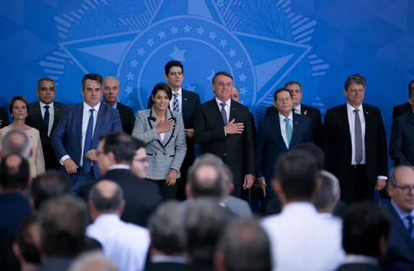 Bolsonaro em cerimônia de despedida aos ministros que serão candidatos nas eleições. Ele leva a mão ao peito ao lado da fileira de ministros e em frente a plateia no Planalto - Metrópoles
