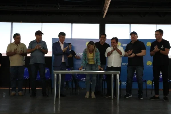 Imagem colorida da vice-governadora do DF, Celina Leão, assinando um papel sob uma bancada. Ao lado dela, estão seis homens