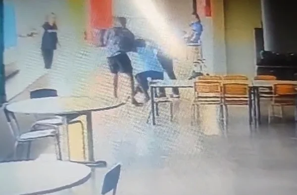 Imagem colorida mostra dois homens segurando adfolescente com camisa azul