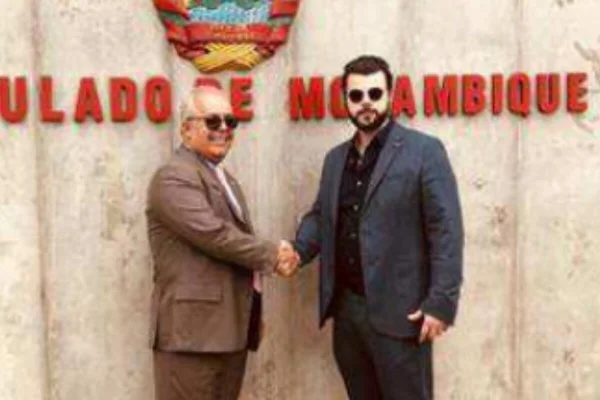 Dois homens vestidos com ternos apertam as mãos, em frente a muro com os dizeres "consulado de moçambique" - Metrópoles