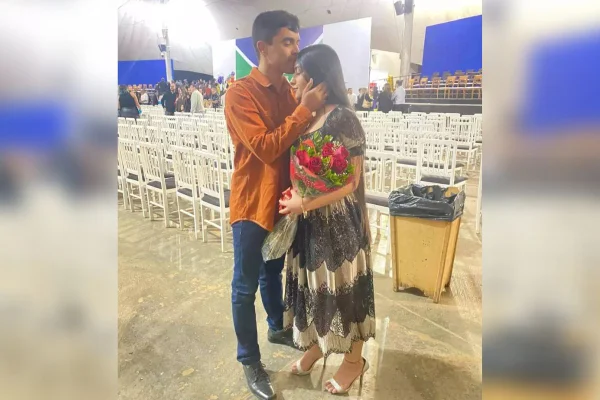 Foto de um homem beijando uma mulher na testa que segura um buque de rosas