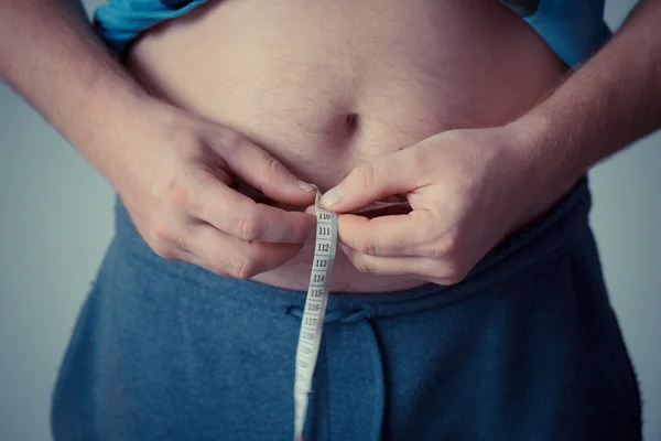 Foto mostra homem medindo a própria barriga com uma fita métrica