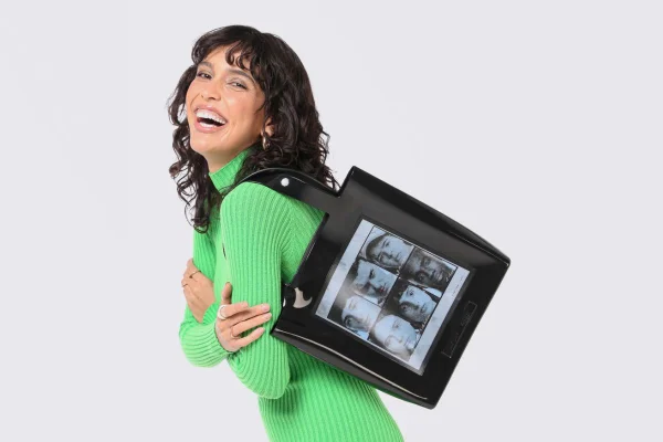 Mulher branca com vestido verde segurando uma bolsa preta