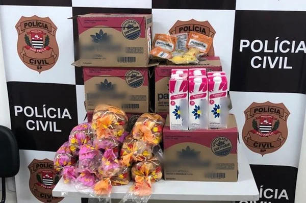 Em foto colorida caixas de leite e embalagens de pão de forma sobre mesa com banner da Polícia Civil de fundo - Metrópoles