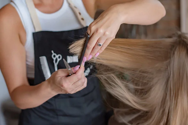 Mulher puxando os fios de um cabelo loiro, ajustando com a mão para cortar com tesoura