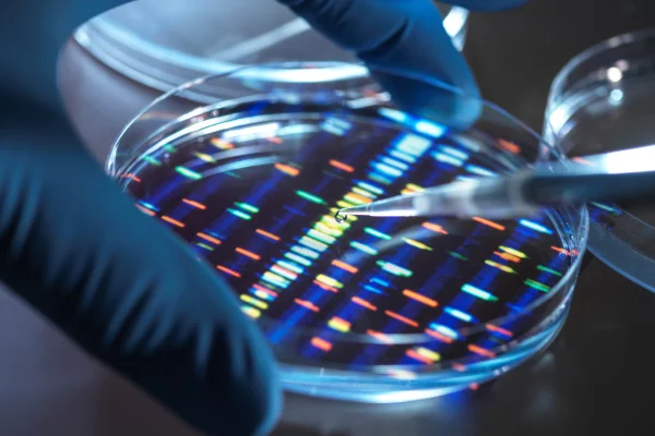 Foto colorida em tons de azul que mostram mão humana com luva em laboratório - Metrópoles.