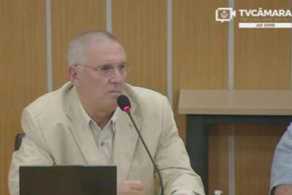 Imagens coloridas mostram homem branco, idoso, calvo, com paletó bege e camisa branca sentado em bancada