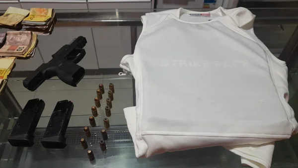Imagem de uma arma, com munições empilhadas e enfileiradas, ao lado de um colete a prova de bala branco - Metrópoles
