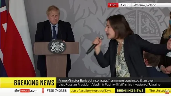 Jornalista ucraniana confronta Boris Johnson. Ela segura um microfone, um pouco a frente do púlpito onde o inglês está - Metrópoles
