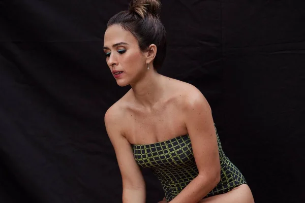 Atriz Tatá Werneck, mulher branca com cabelo preto preso em coque, posando para foto. Ela usa um maiô cinza com listras verdes claras. A peça é da marca ESC.