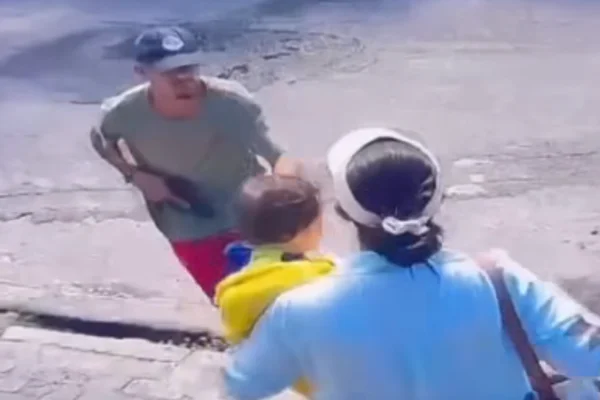 Imagem colorida de suspeito armado abordando mulher com bebê no colo. Metrópoles