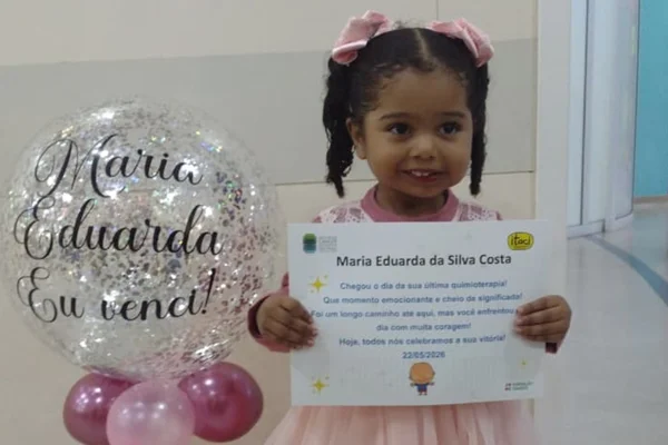 Foto colorida de criança segurando um certificado de "venci o câncer" - metrópoles.