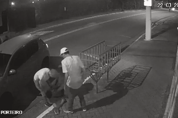 Imagem de uma câmera de segurança mostra três homens agredindo e apontando uma arma no rosto de outro jovem derrubado na calçada - Metrópoles