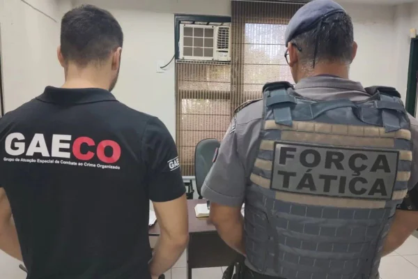 Imagens coloridas mostram dois homens de costas, um deles com camiseta preta e a inscrição GAECO, em vermelho, outro com com uniforme da PM e colete balístico com inscrição Força Tática
