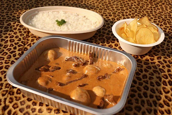 na foto vemos uma travessinha de aluminio com estrogonofe de carne e atras dela duas cumbucas brancas, uma com arroz e outra com batatas chips
