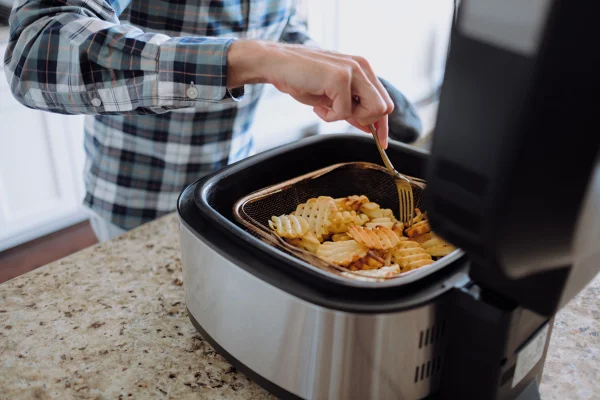 Close-up de um homem branco irreconhecível cozinhando batatas fritas com waffle na fritadeira de ar