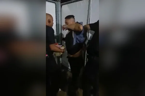 vigilante levanta camiseta de homem enquanto outro segura celulares