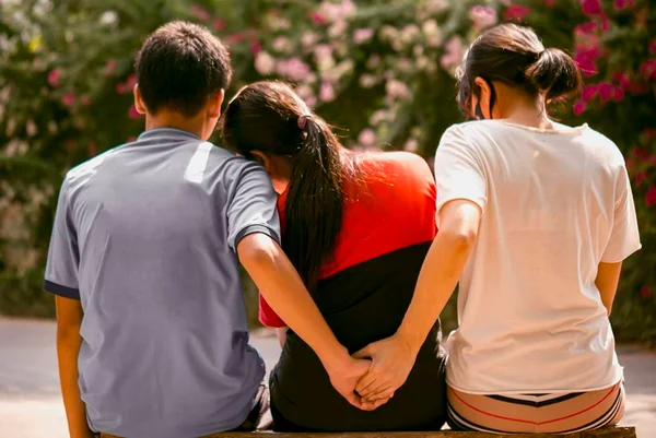 Três pessoas sentadas de costas, com as duas das pontas dando as mãos - Metrópoles