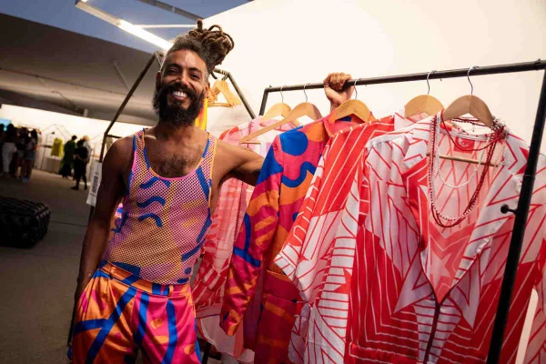 Homem negro em frente a arara usa peças coloridas da marca Cabaré Amazônico - Metrópoles