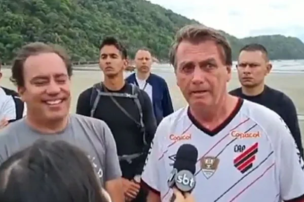 Na foto temos ao fundo uma praia, e na frente o presidente jair bolsonaro e algumas pessoas ao redor