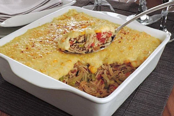 Na foto vemos uma travessa branca com peru desfiado coberto por creme amarelo de milho gratinado