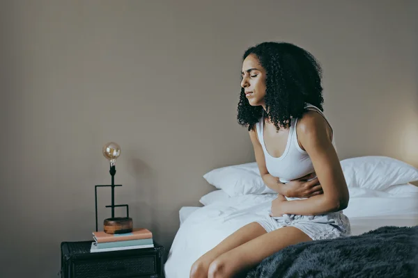 Foto colorida de mulher sentada na cama com dor de barriga - Comeu demais? Saiba como o corpo reage e o que ajuda a se recuperar - Metrópoles