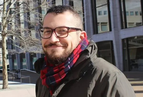 foto colorida de homem com casaco preto e cachecol vermelho