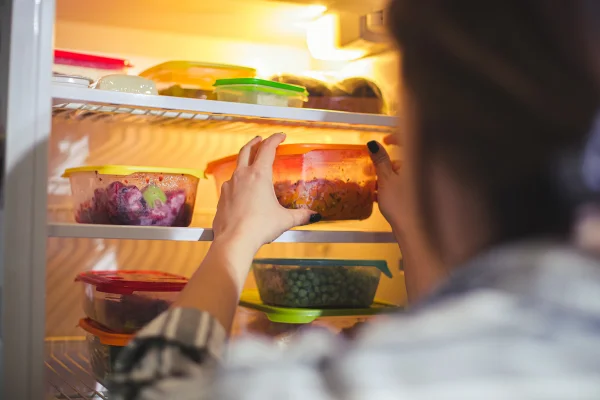Imagem mostra mulher guardando potes de vidro tampados com comida na geladeira - Metrópoles